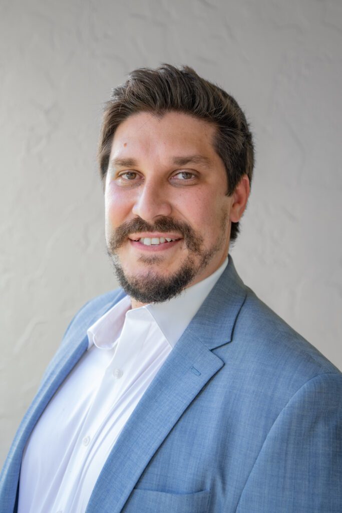 A man in a suit and beard smiling for the camera.