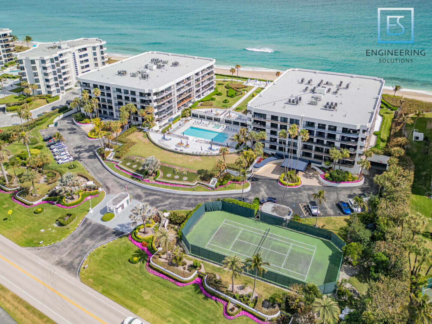 A view of the ocean from above shows tennis courts, beach and buildings.