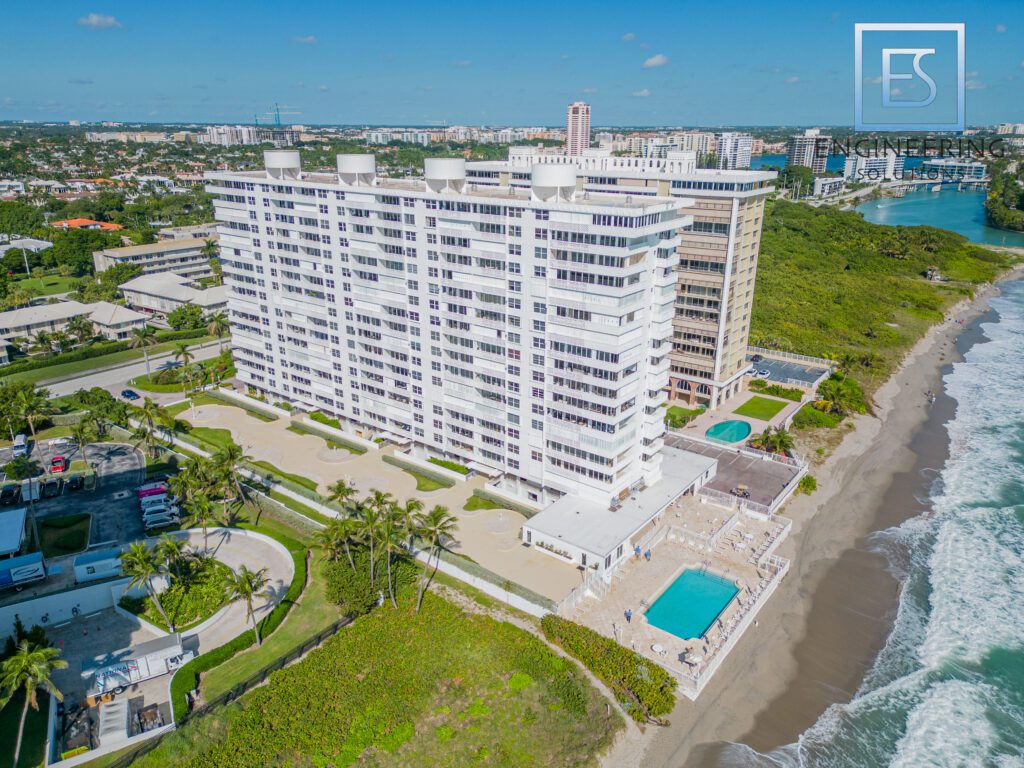 A large white building with pools and a beach in the background.